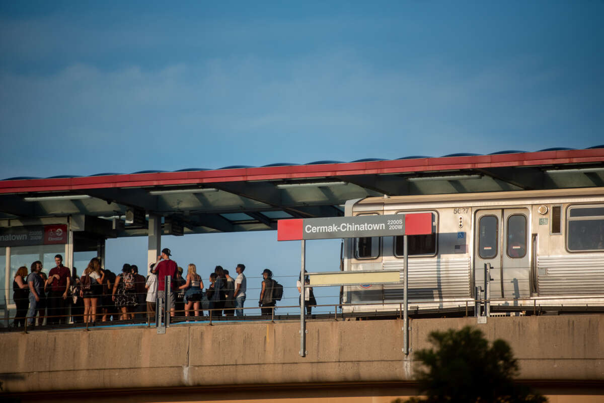 A crowd of people waits on the Cermak-Chinatown Red Line CTA platform as a train approaches.