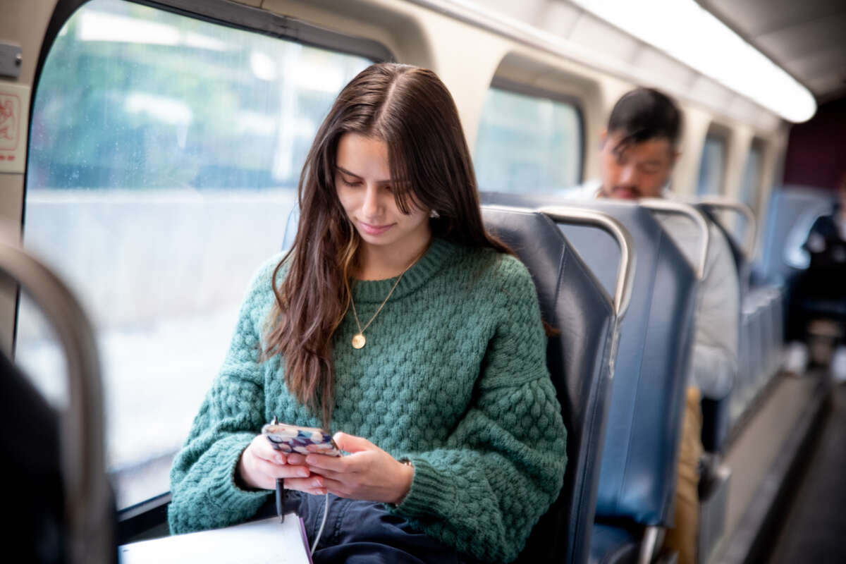 A young woman in a green sweater looks at her smartphone on a Metra train.