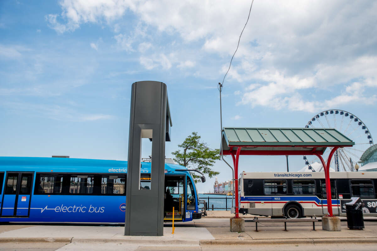 Electric bus and CTA bus parked at Navy Pier bus turnaround with Ferris Wheel visible in background.
