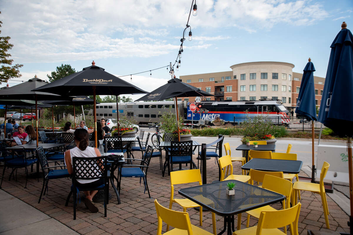 People dining at an outdoor cafe with a Metra train in the background.