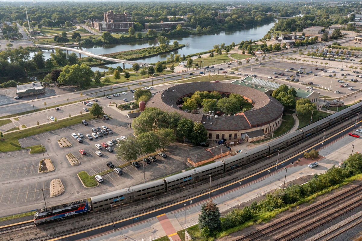 A Metra train at the round Aurora station with a pedestrian bridge over water in the background.
