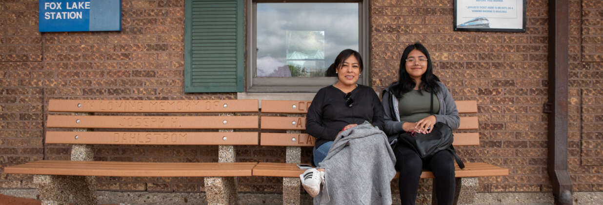 Two women sit on a bench at the Fox Lake Metra station.