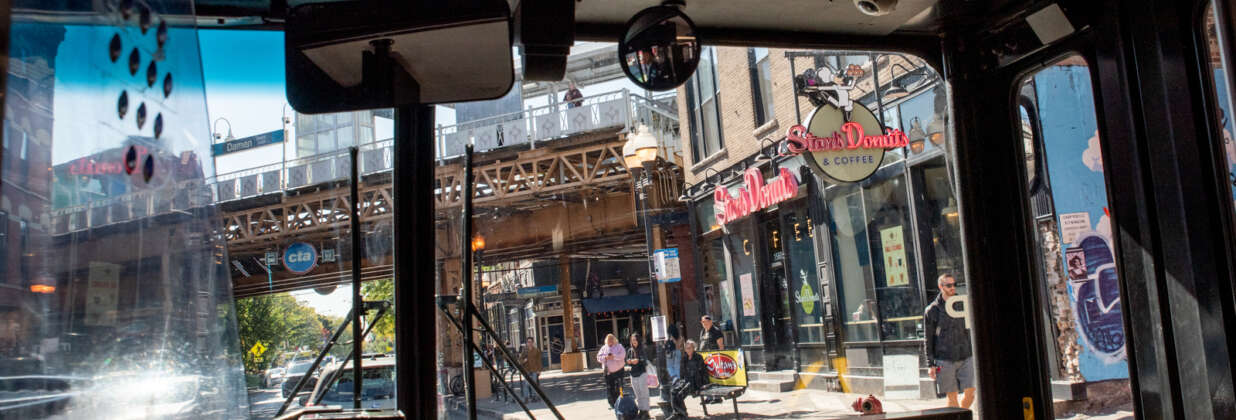 View out the front window of a CTA bus of the Blue Line tracks and people waiting at the bus stop.