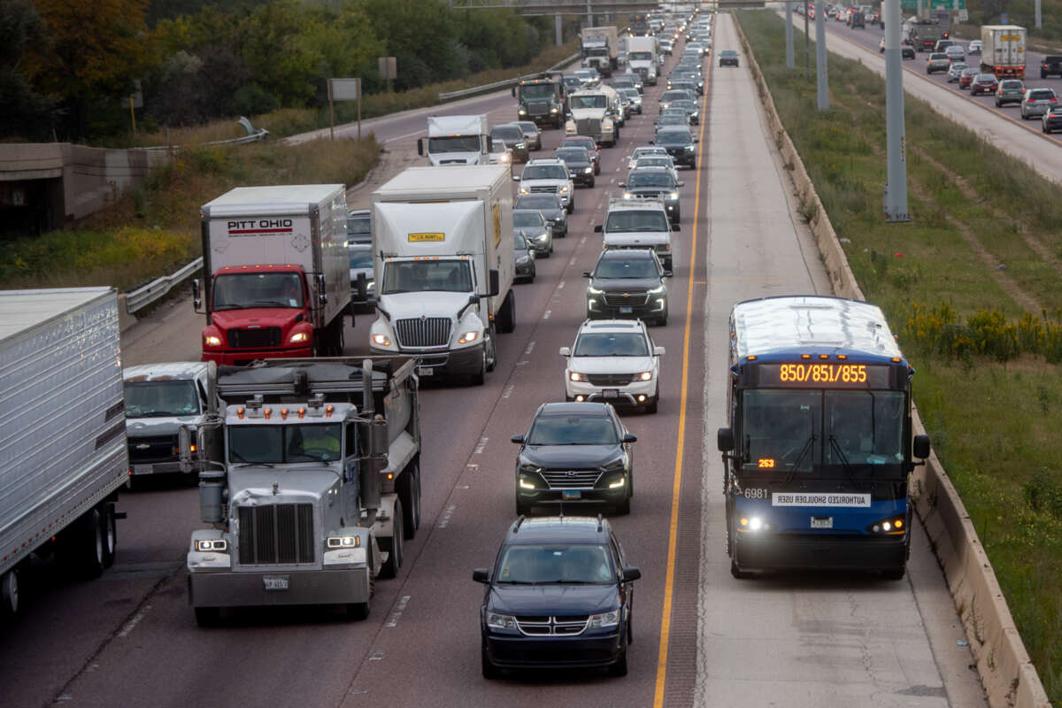 Cars and trucks driving on the highway with a bus in its own lane.