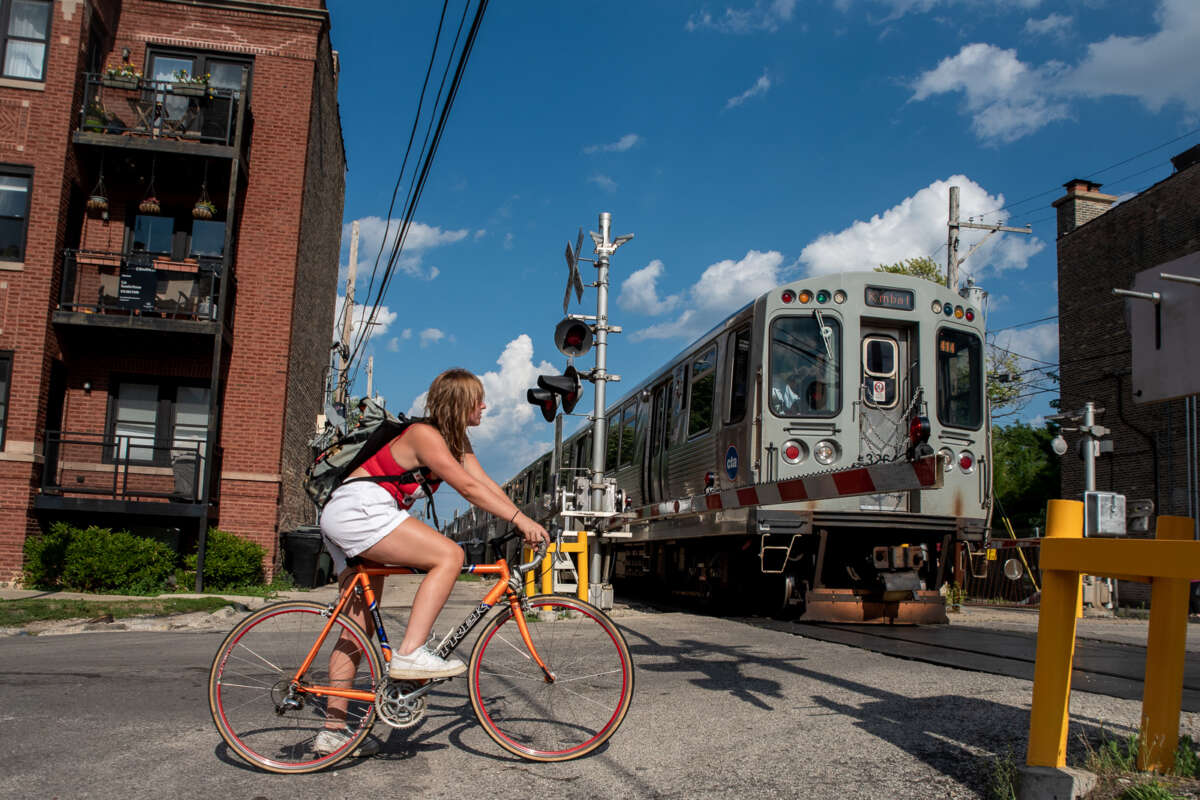 Woman on bike at a railroad crossing waiting for Brown Line train to pass.