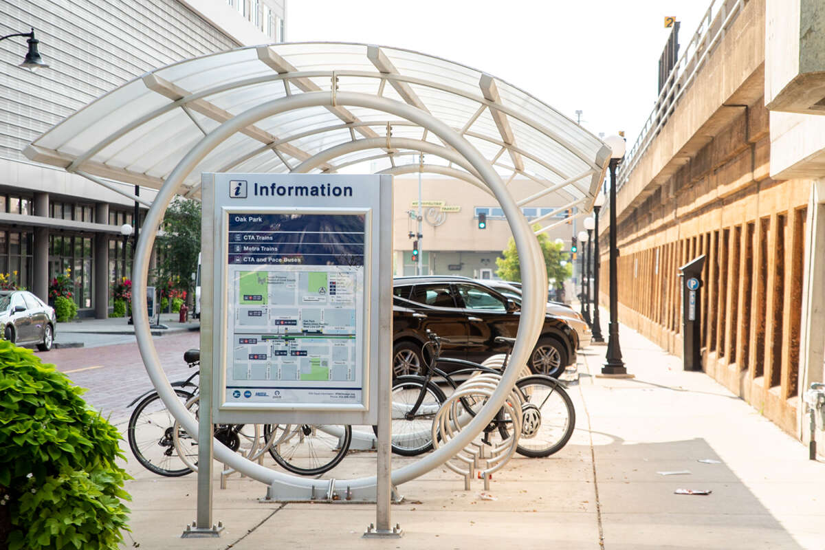 Covered bicycle racks with two bicycles with a map and information sign about Oak Park, outside of a train station.