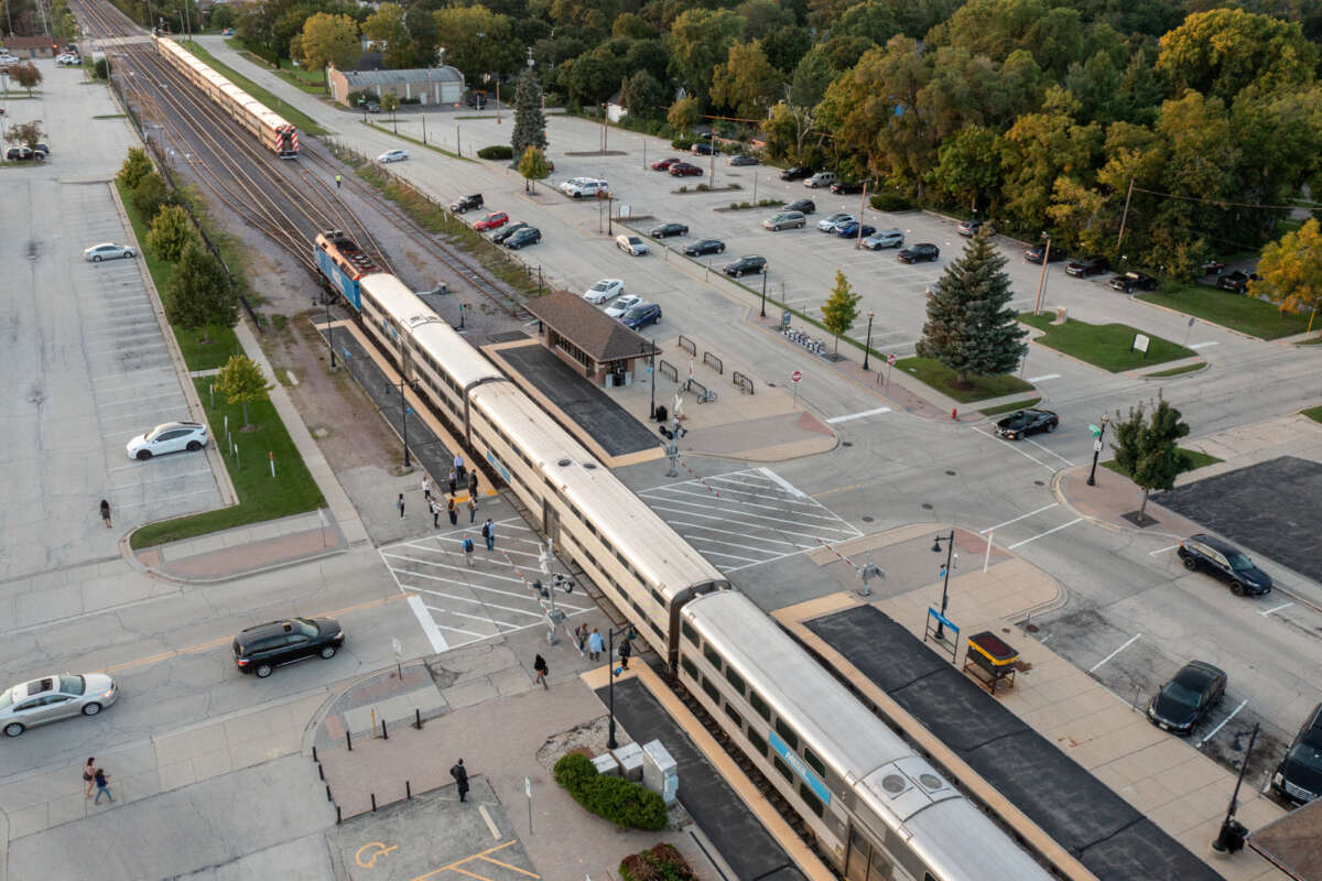 A Metra train at a station with a mostly-empty parking lot.